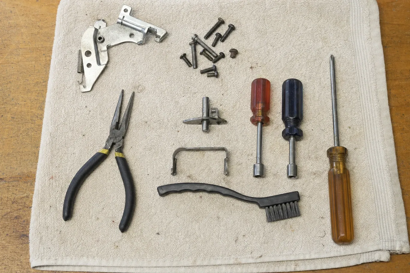 Door hinge assembly and its spring laid out on a shop towel with nut drivers, pliers, a wire brush and screws